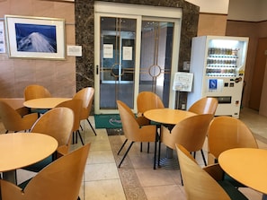 A cafe with wooden tables and chairs, a vending machine, and a framed picture of a mountain. - Toyoko Inn Tokyo Haneda Kuko No.1 (Tokyo)