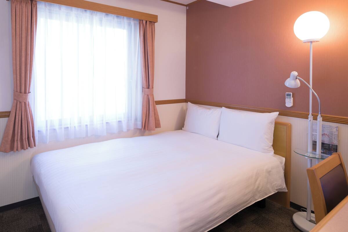 A hotel room with a large bed, a bedside table with a lamp, and a window with curtains.