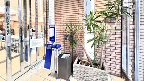 A hotel entrance with a brick wall, a glass door, a blue payment machine, and potted plants.