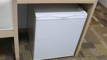 A white Toshiba refrigerator under a wooden desk with a carpeted floor.