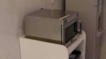 Una cocina compacta con un microondas sobre una encimera blanca, un lavamanos pequeño y un mueble debajo.