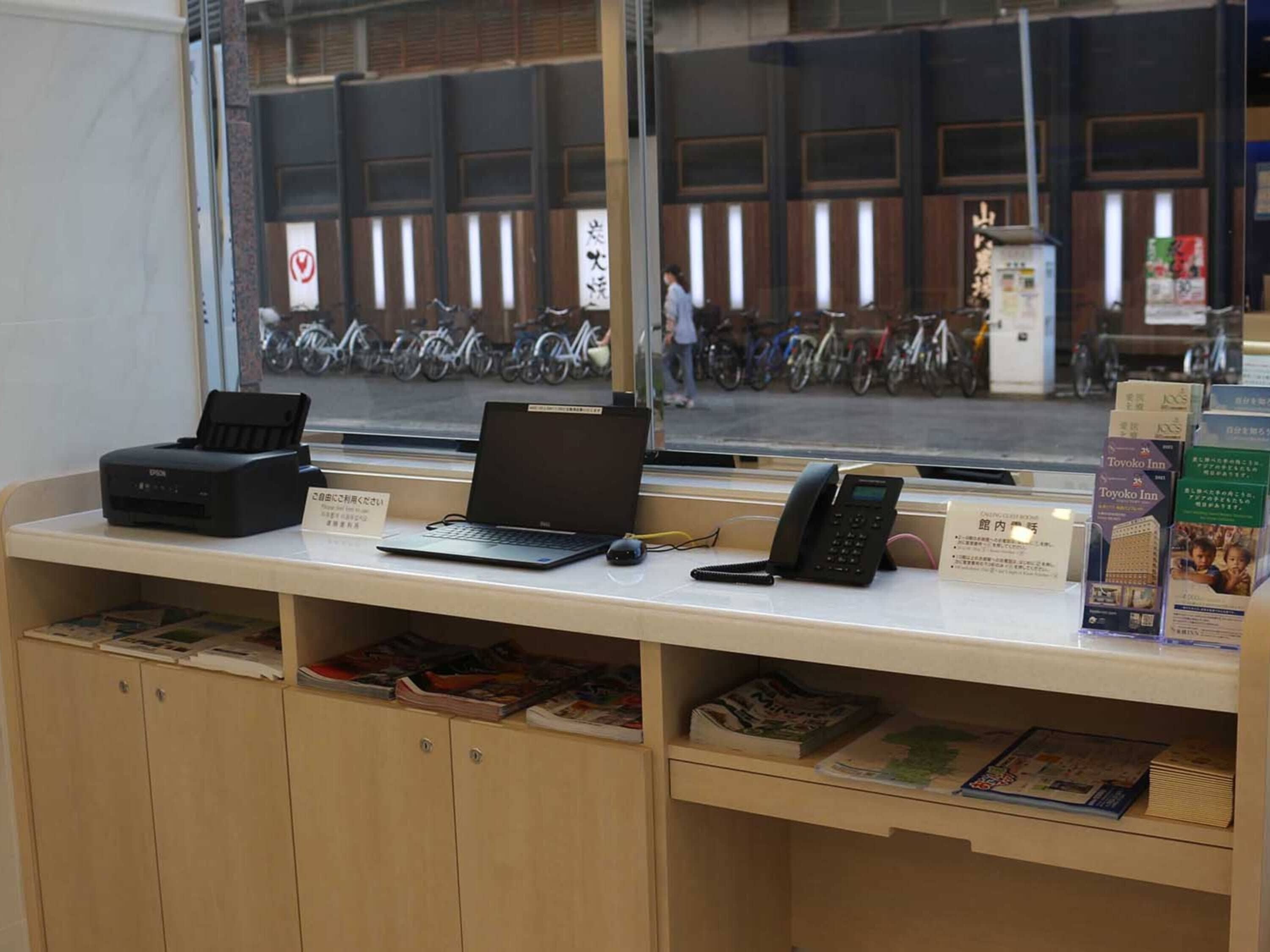 Un mostrador de recepción con computadora, teléfono y folletos.