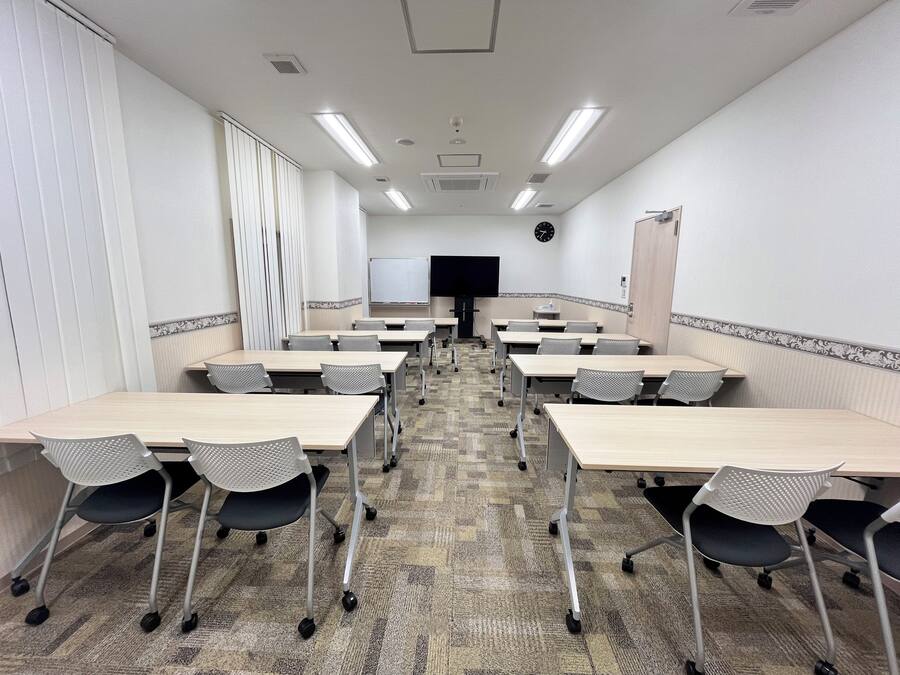 A conference room with multiple tables and chairs, a whiteboard, a clock, and a television on the wall.