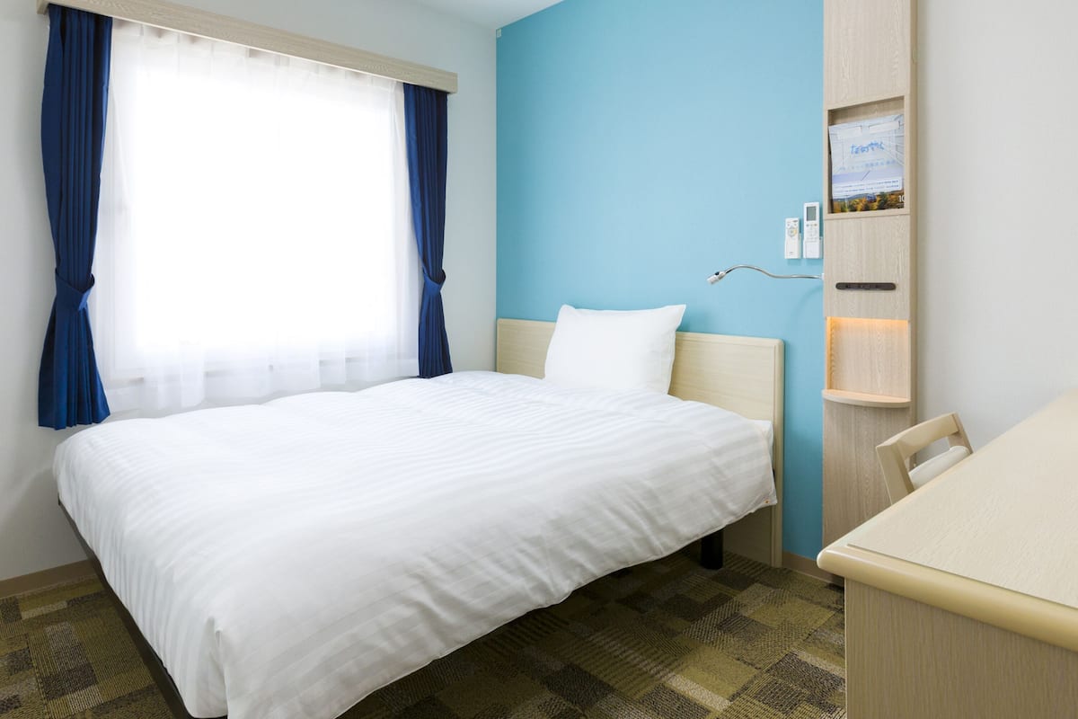 A hotel room with a bed, a desk, and a window with curtains.