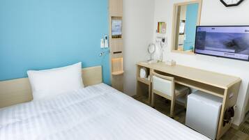 A hotel room with a bed, a desk with a chair, a small refrigerator, a mirror, a clock, and a TV on the wall.