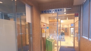 A hotel entrance with a glass door, a sign indicating it is part of the INN chain, and a green information kiosk. - Toyoko Inn Osaka Hommachi No.1 (Osaka)