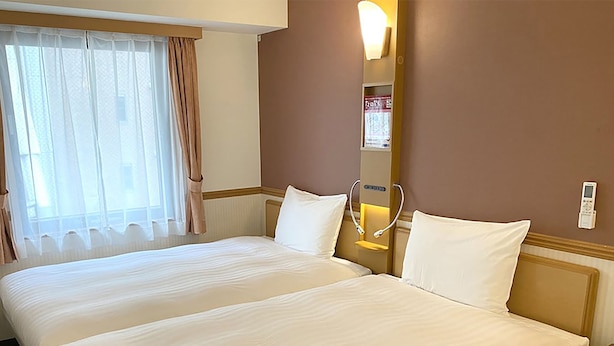 A hotel room with two beds, a bedside table, a nightstand, a lamp, and a window with curtains. - Toyoko Inn Osaka Hommachi No.1 (Osaka)