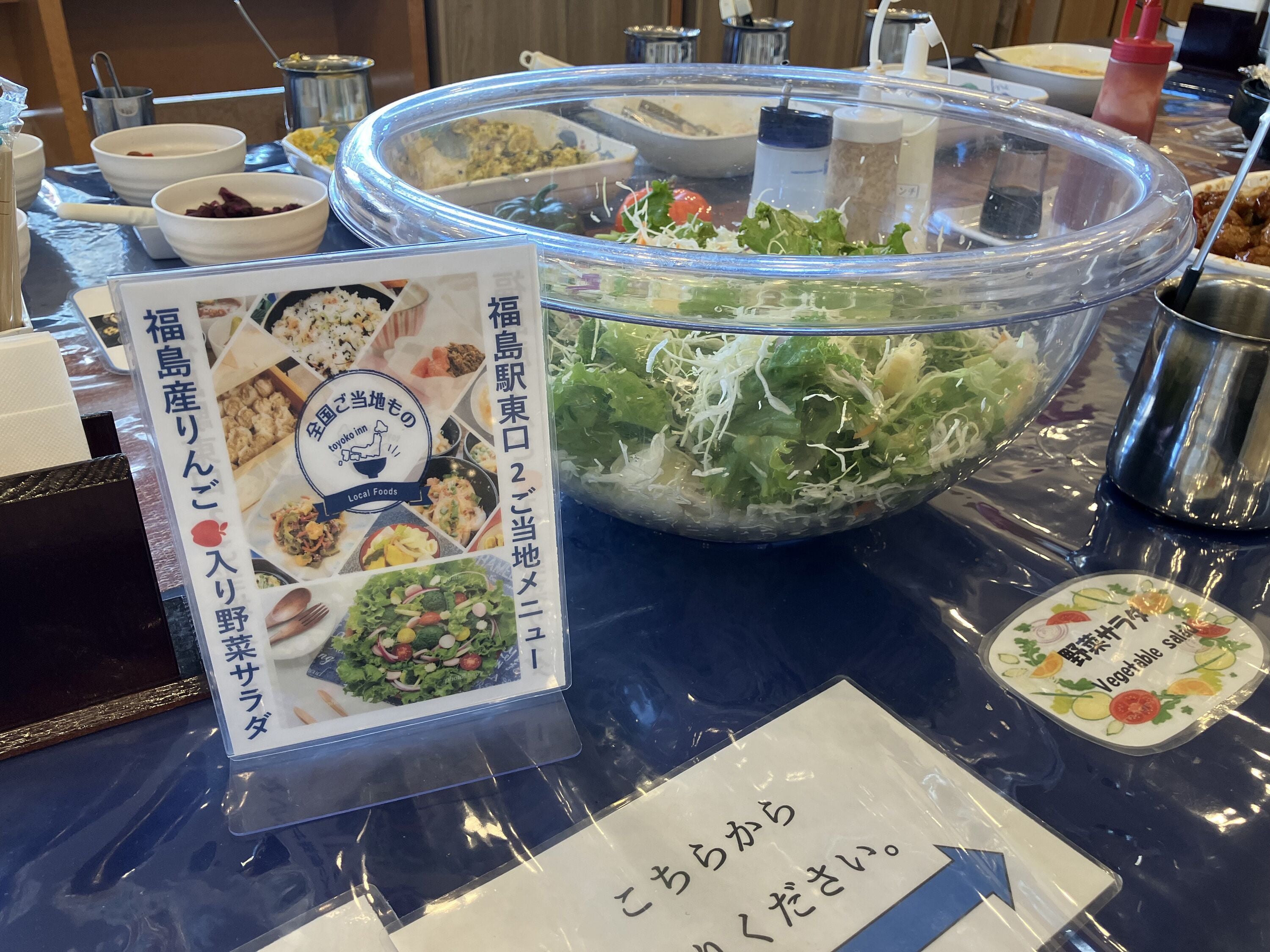 Une table de buffet proposant divers plats, notamment des salades et d’autres aliments, ainsi qu’un panneau indiquant « Produits du terroir ».