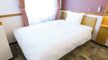 A hotel room with a large bed, a bedside table, a lamp, and a window with curtains.
