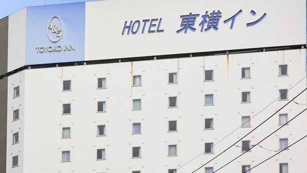 Egy szállodai épület, amelyen egy „TOYOKO INN HOTEL 東横イン” feliratú tábla található.