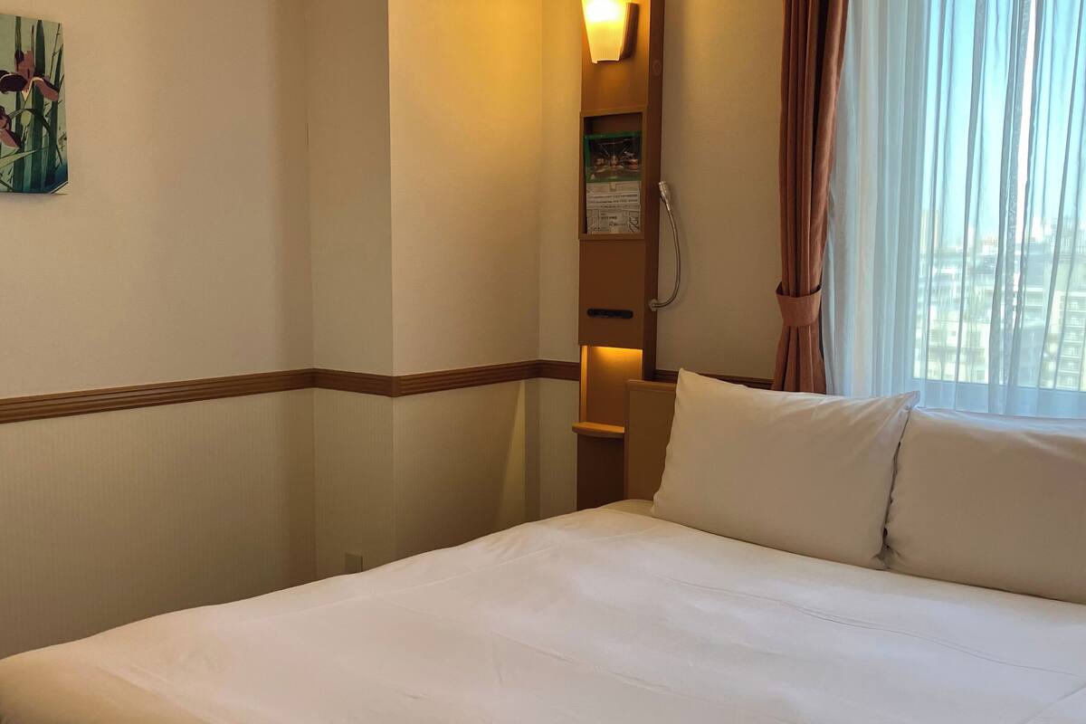 A hotel room with a bed, a nightstand, a lamp, and a window with curtains.