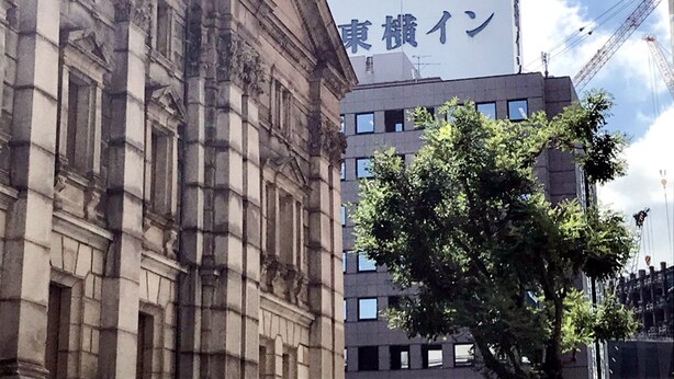 Un hôtel avec une enseigne en anglais et en japonais, un arbre devant et une grue de construction en arrière-plan.