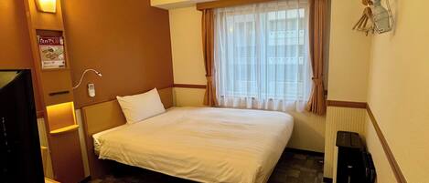 A hotel room with a bed, a TV, a desk, and a window with curtains.
