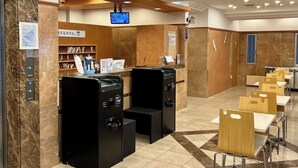 Ein Hotel-Empfangsbereich mit Marmorwand, Holzbüro, einem digitalen Bildschirm und einer Sitzecke mit Holztischen und -stühlen.