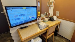 Ein Hotelzimmer mit Schreibtisch, Fernseher mit Speisekarte, Telefon, Spiegel und kleinen Mülleimer.