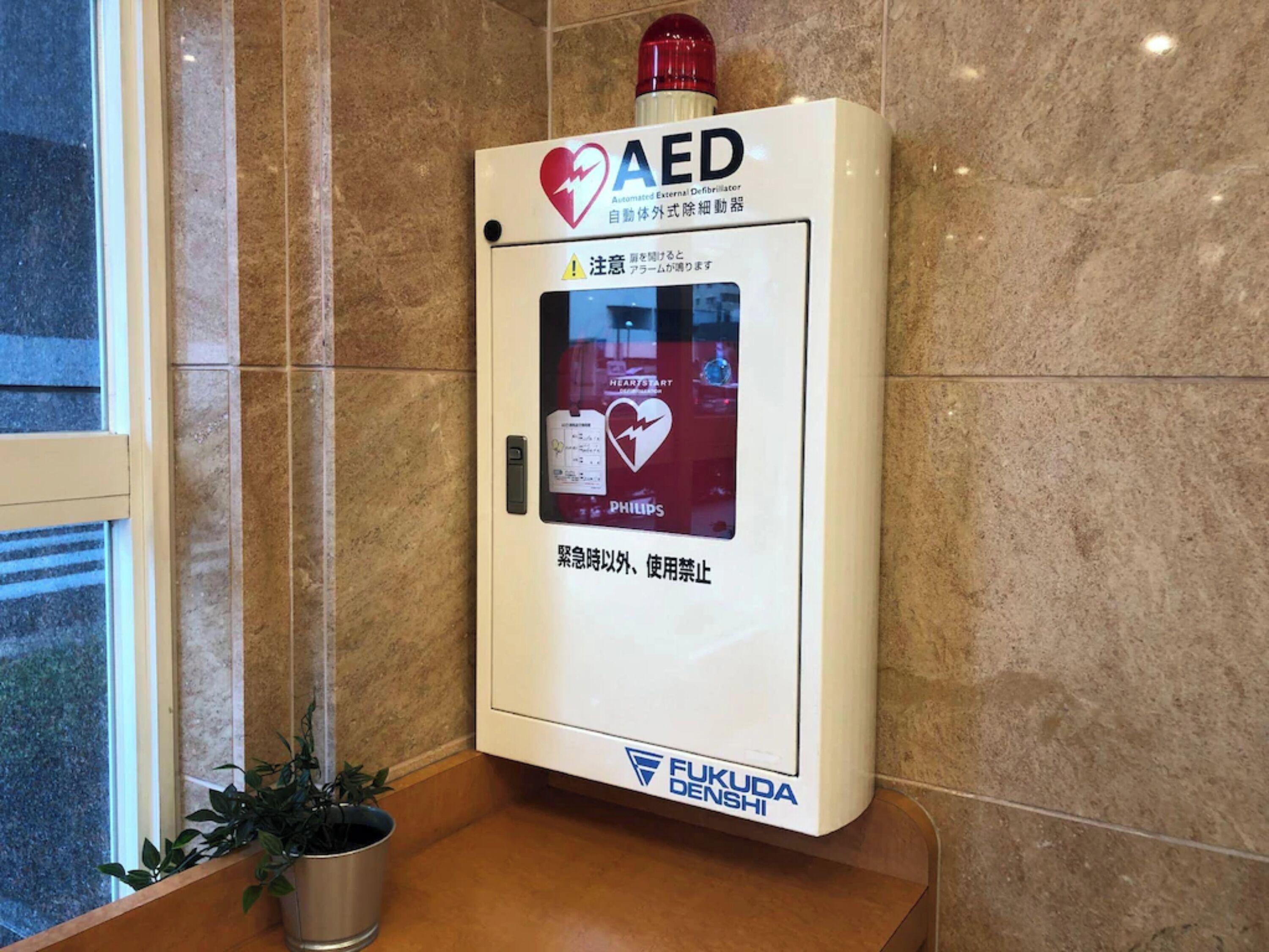 An AED device mounted on a wall with a warning sign and instructions in Japanese.