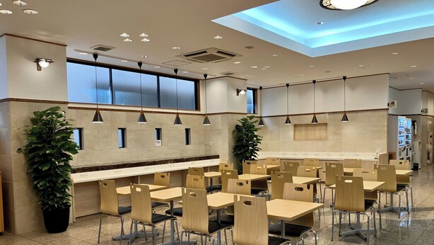Un área de comedor moderna con varias mesas y sillas, una larga barra y plantas en macetas.