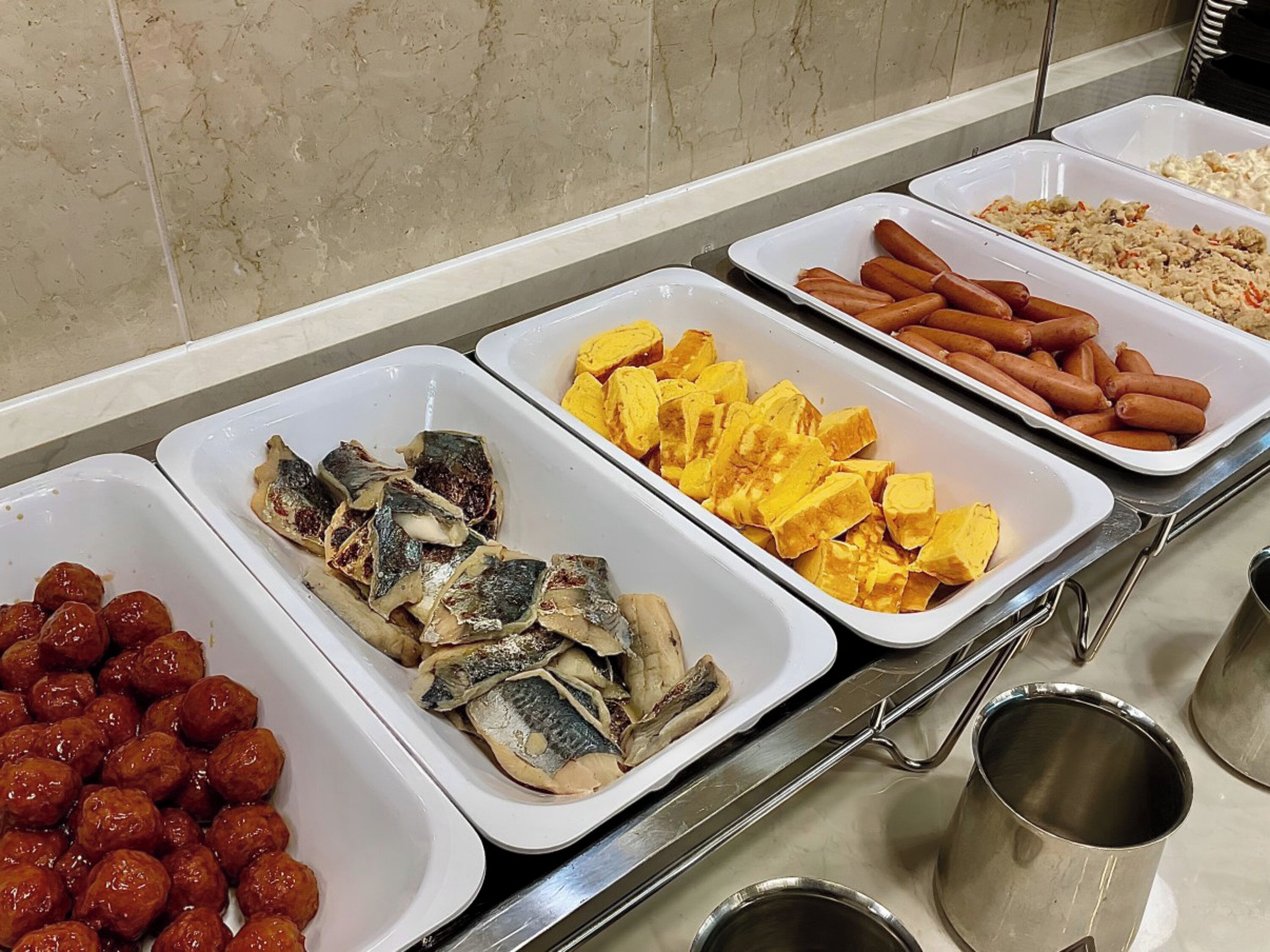 Un buffet proposant une variété de plats, notamment du poisson, des saucisses et d’autres spécialités.