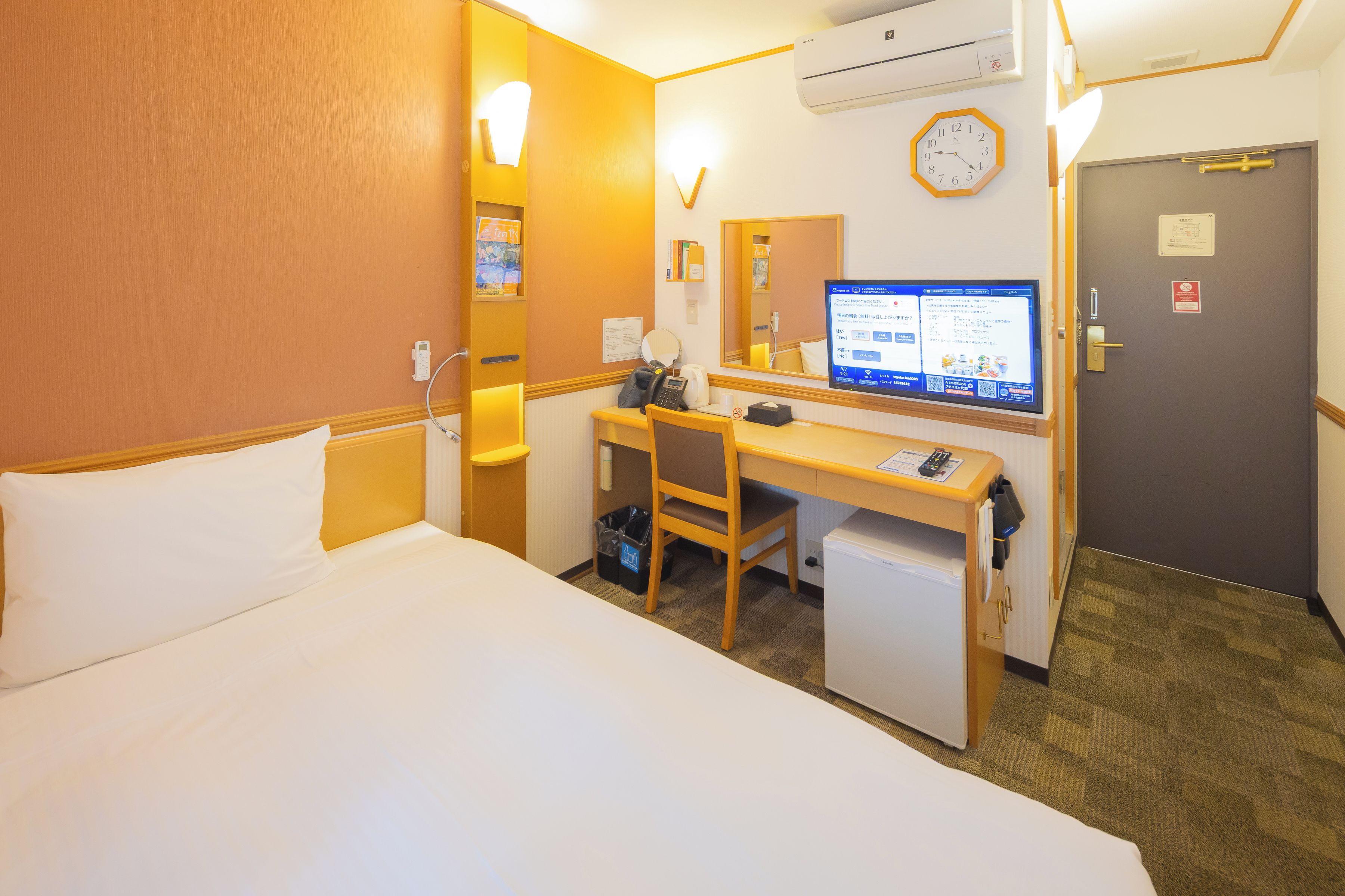 A hotel room with a bed, desk, chair, and a television displaying a menu.