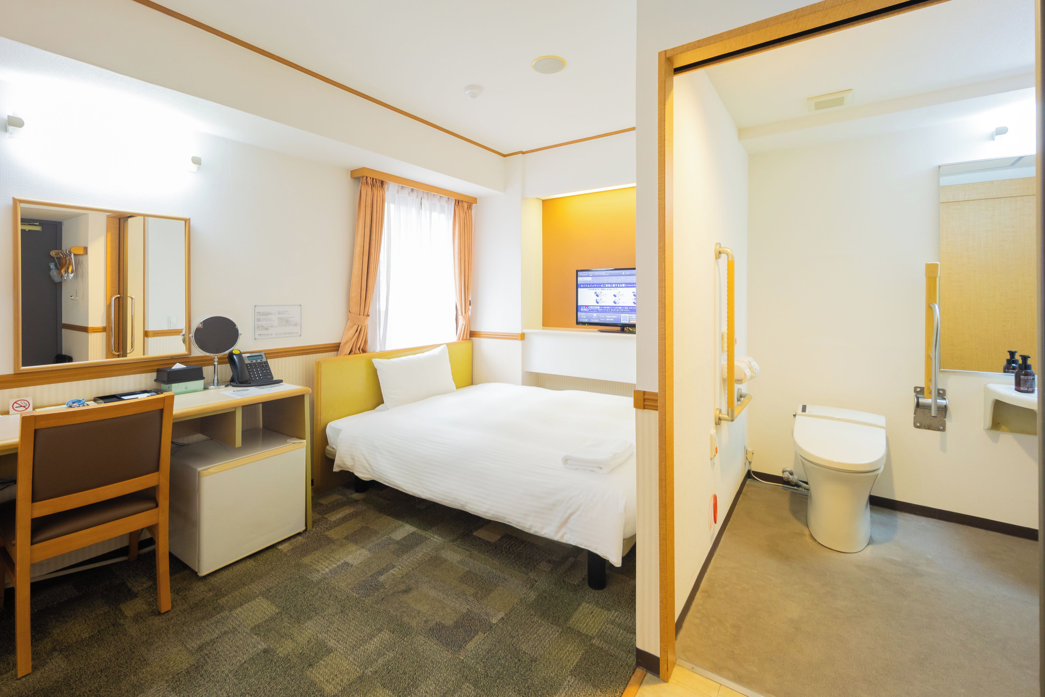 A hotel room with a bed, desk, chair, and a bathroom with a toilet and sink.