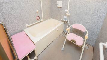 A bathroom with a bathtub, a pink stool, a handrail, and a shower chair.