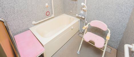 A bathroom with a bathtub, a pink stool, a handrail, and a shower chair.