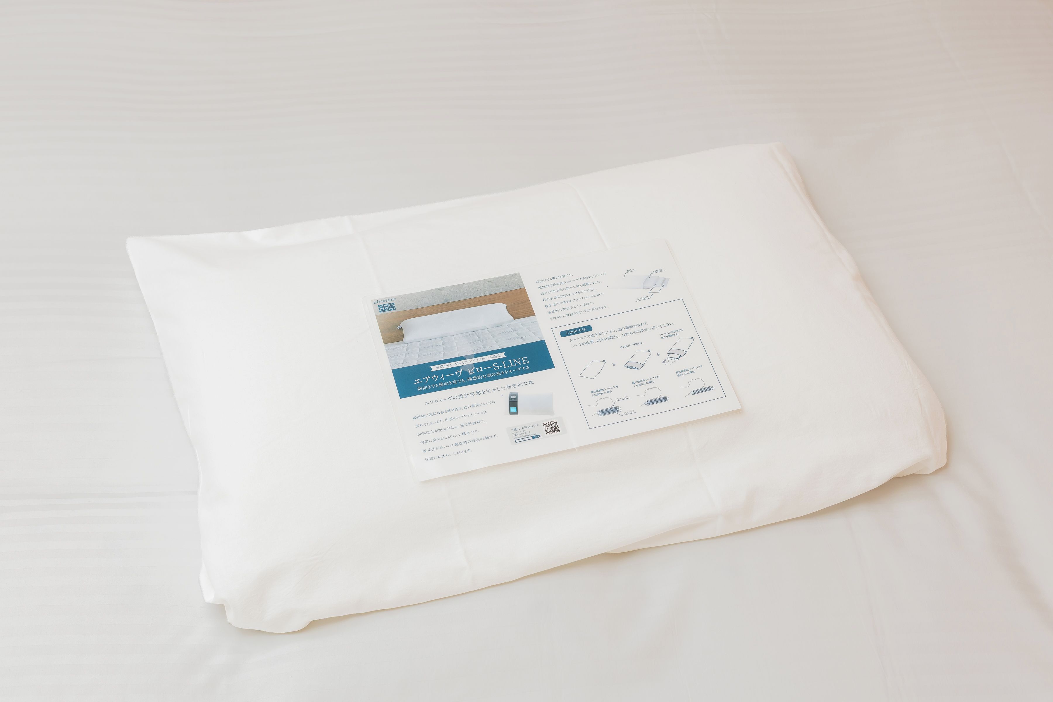 A neatly folded white pillow with a printed tag on a white bedspread.