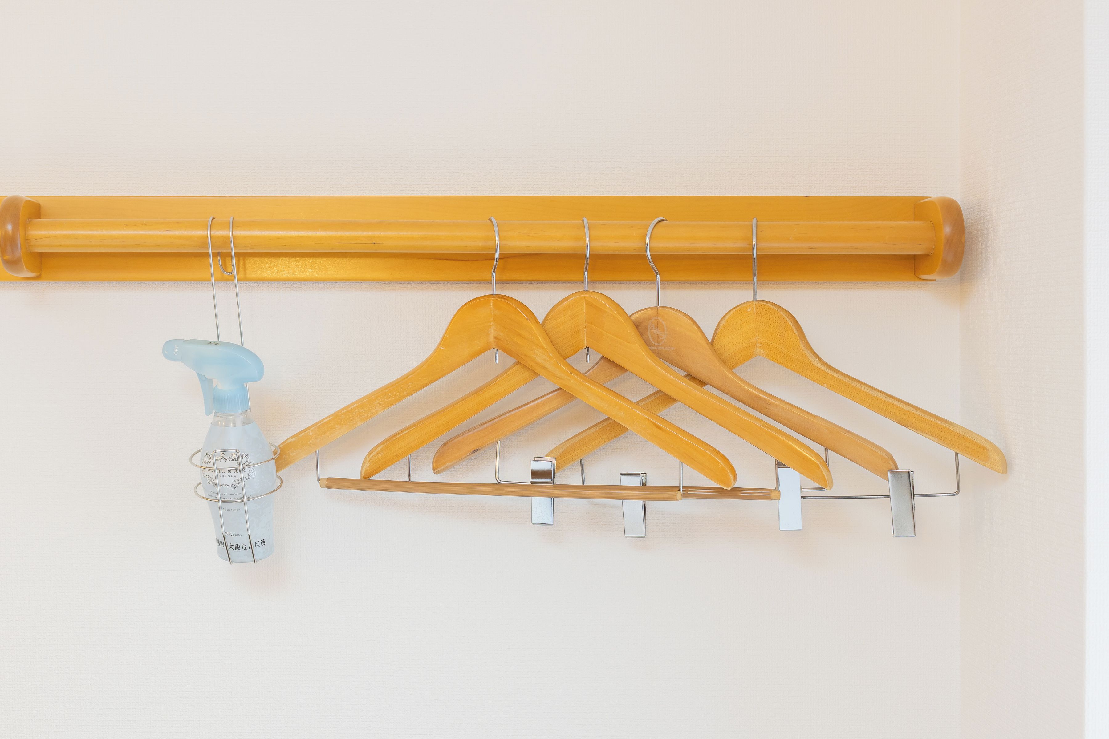 A wall-mounted wooden hanger rack with multiple hangers and a spray bottle.