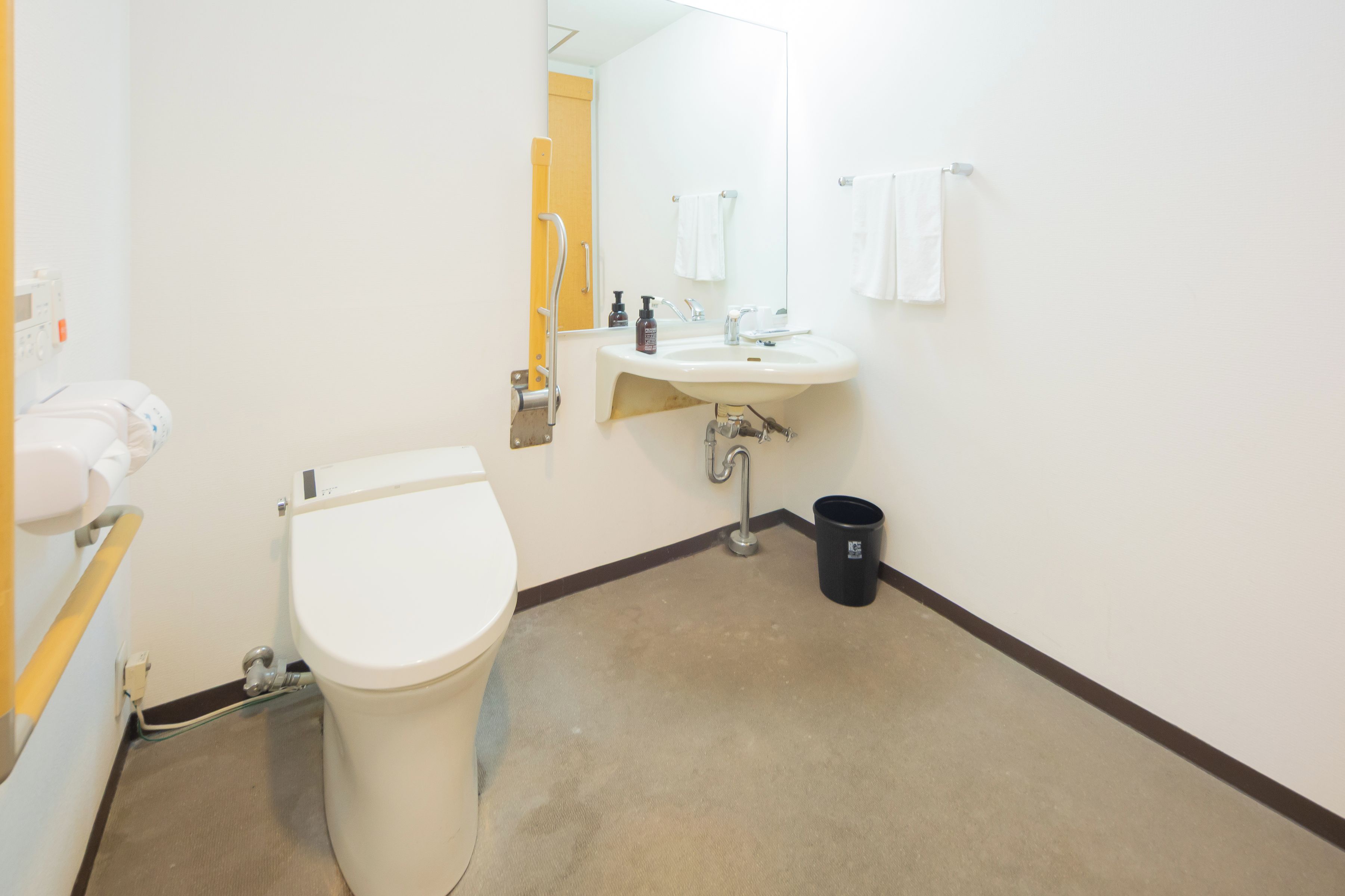 Une salle de bain d’hôtel standard, équipée de toilettes, d’un lavabo et d’une poubelle.