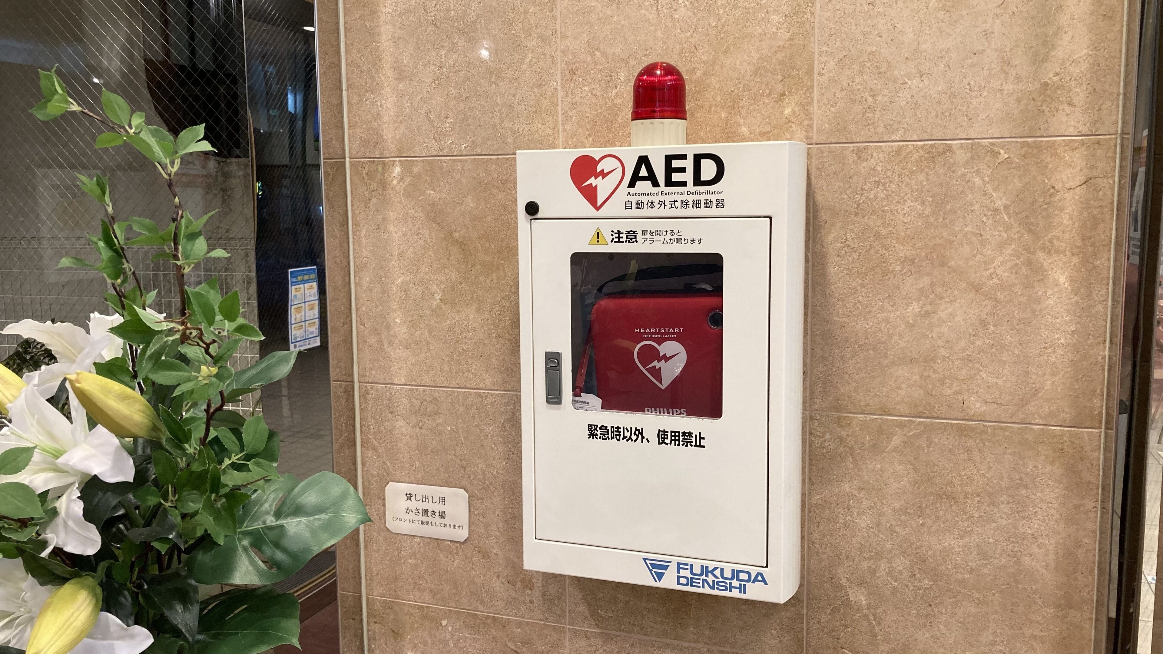 Uma caixa de DEA (Desfibrilador Externo Automático) fixada em uma parede com uma luz de emergência vermelha acima.