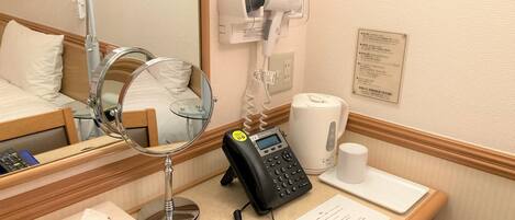 Une chambre d’hôtel comprenant un lit, une table de chevet avec une lampe, un téléphone, un miroir et un sèche-cheveux fixé au mur.
