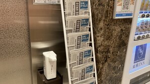 A magazine rack with newspapers, a white trash bin, and a QR code on a wall. - Toyoko Inn Okinawa Naha Kokusai Dori Miebashi Station (Naha)
