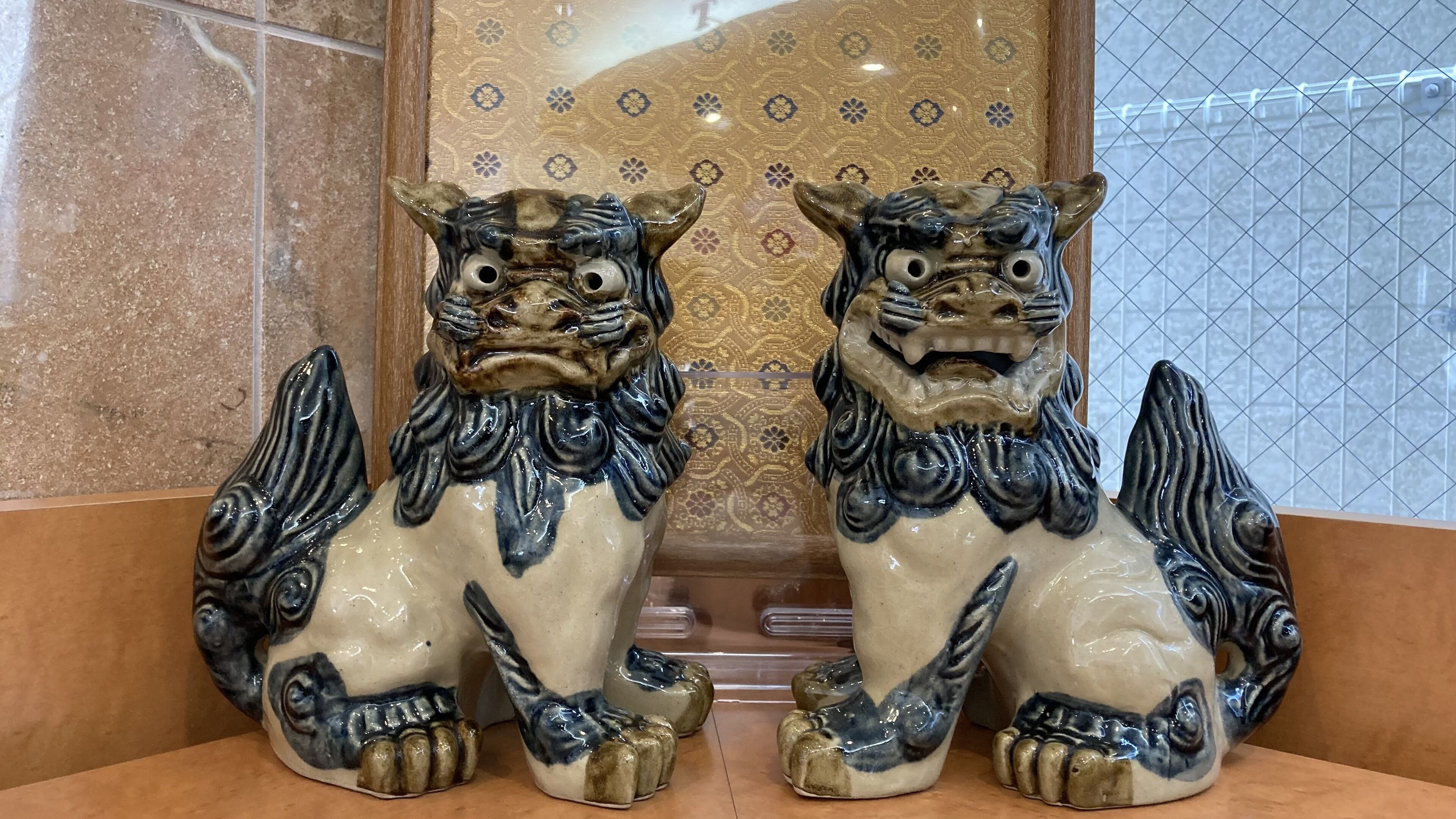 Two ceramic lion statues with intricate designs, placed on a shelf against a patterned wall.