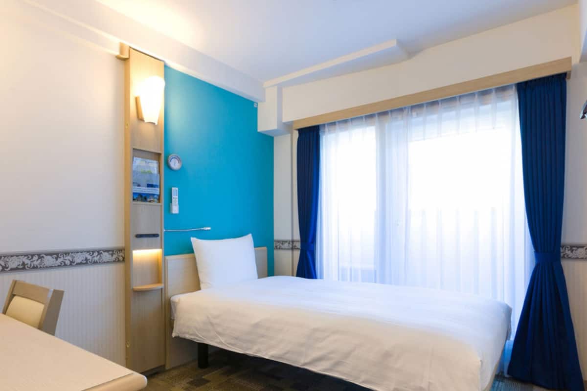 A hotel room with a bed, a desk, and a window with curtains.