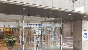 A modern building entrance with glass doors, a blue mat, and a flower arrangement. - Toyoko Inn Utsunomiya Ekimae No.1 (Utsunomiya)
