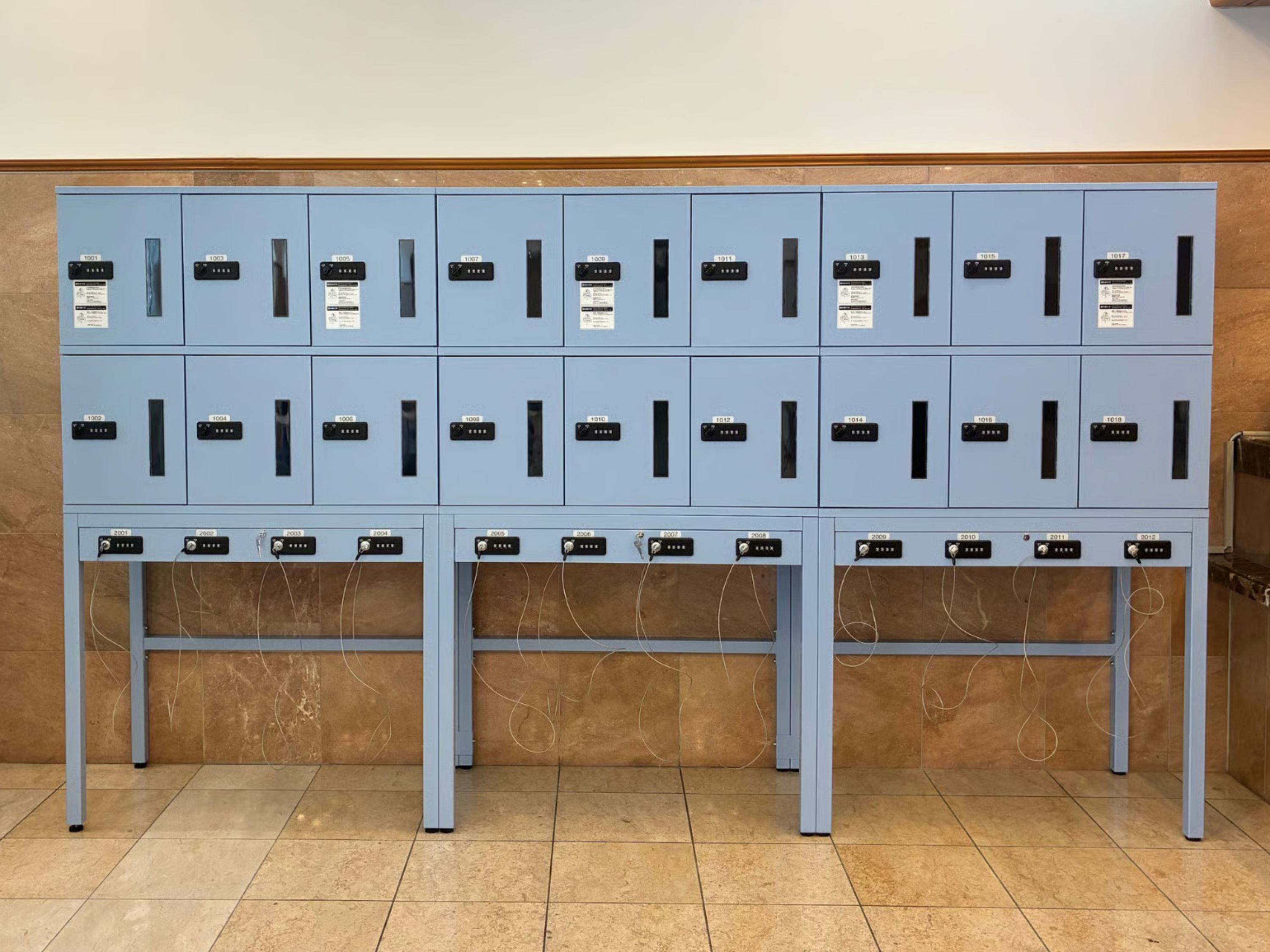 Une rangée de casiers bleus, chacun portant une étiquette numérotée, un petit panneau et un cadenas.