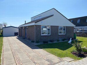 A single-story house with a sloped roof, a visible number '16' on the side, and a small garden with a white bird.