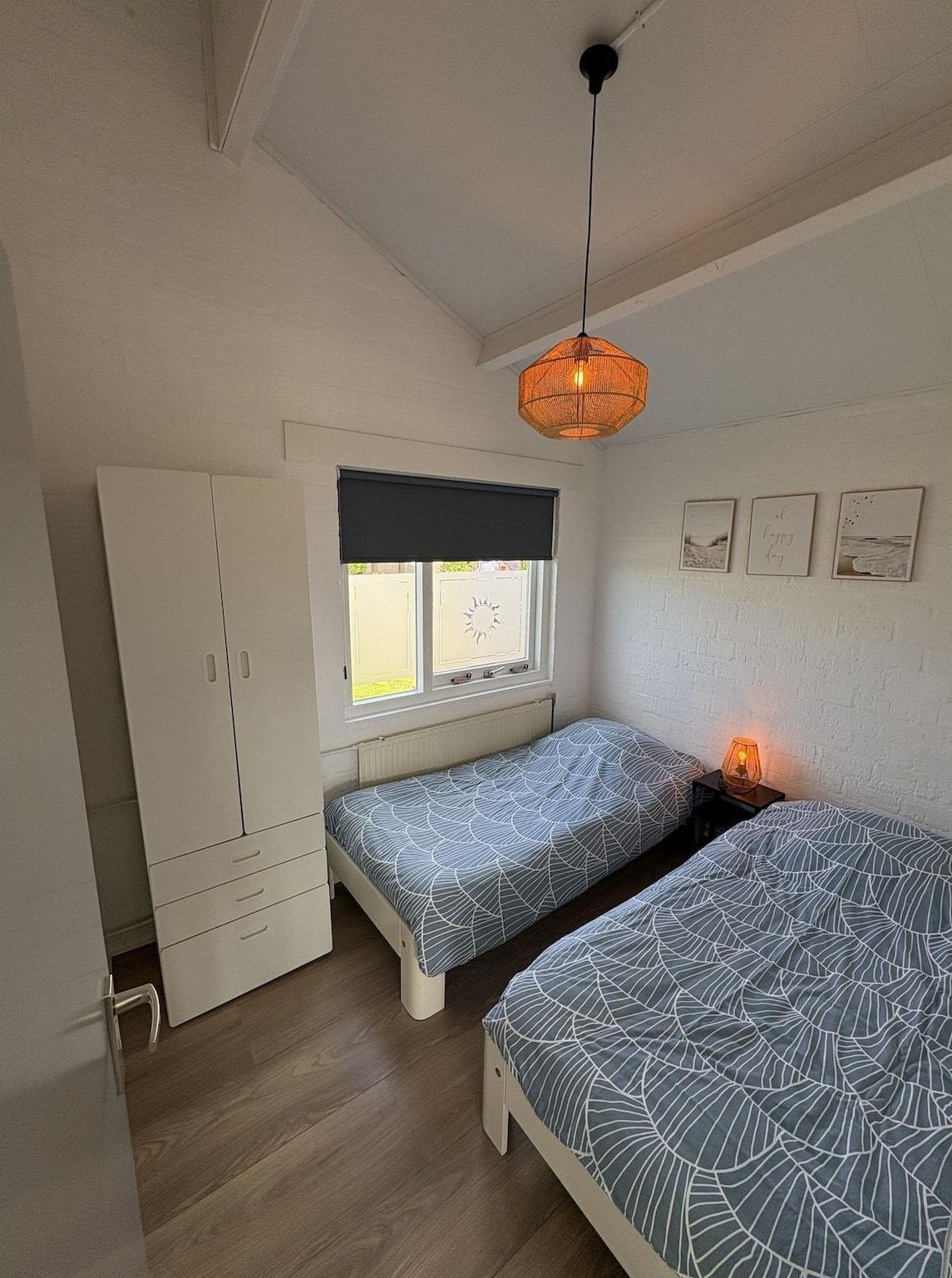 Een slaapkamer met twee eenpersoonsbedden, een kledingkast, een raam met uitzicht en een hanglamp.
