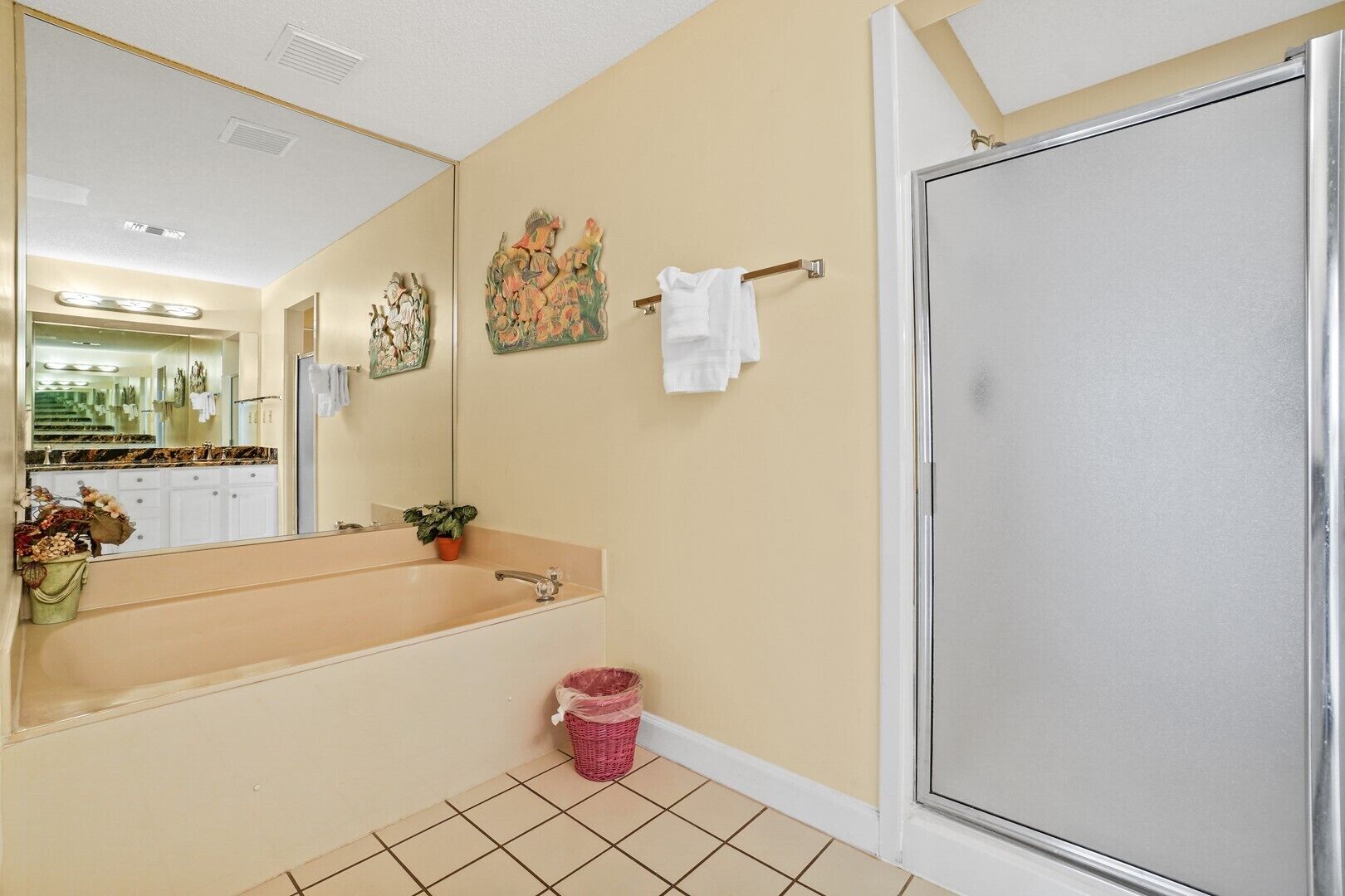 A bathroom with a large mirror, a sink, a shower, and a small trash bin.