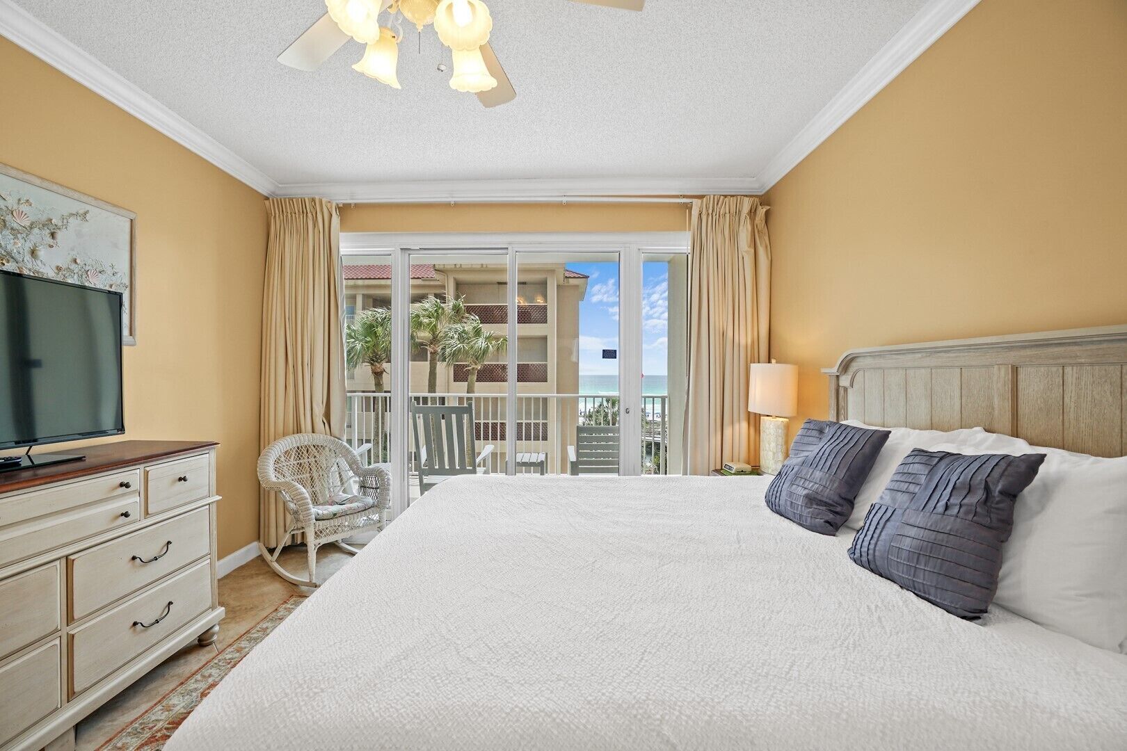 Habitación de hotel con una cama grande, televisión, balcón con vista al océano y una silla.