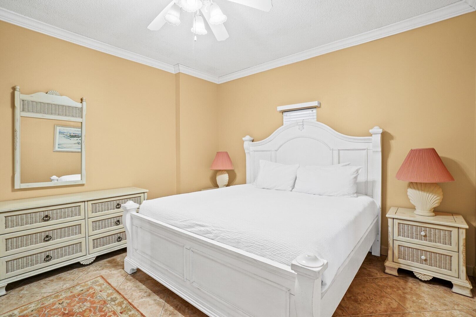 Une chambre à coucher avec un lit blanc, deux tables de chevet avec des lampes, un grand miroir et une commode.