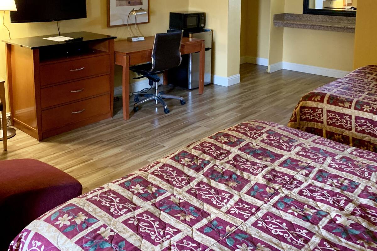 A hotel room with a desk, chair, television, microwave, and two beds with floral bedding.
