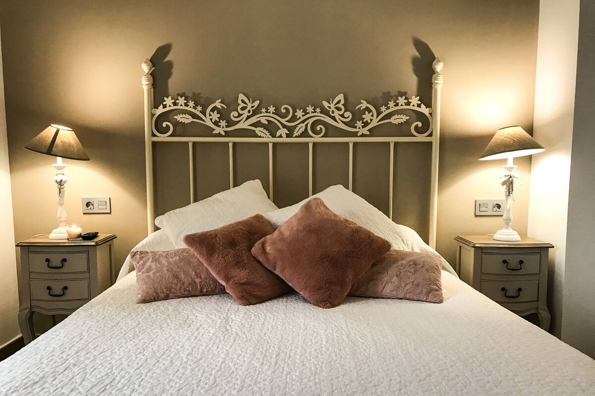 Cama bem arrumada com duas almofadas, cabeceira decorativa e abajures sobre os criados-mudos.