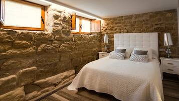Une chambre avec un mur en pierre, un lit doté d’une tête de lit blanche et un plancher en bois.