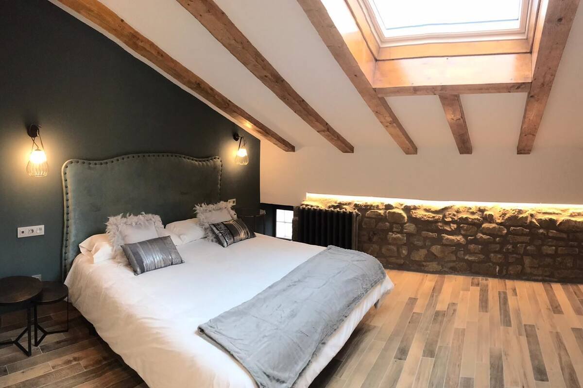 Quarto com uma cama grande, parede de pedra e claraboia.