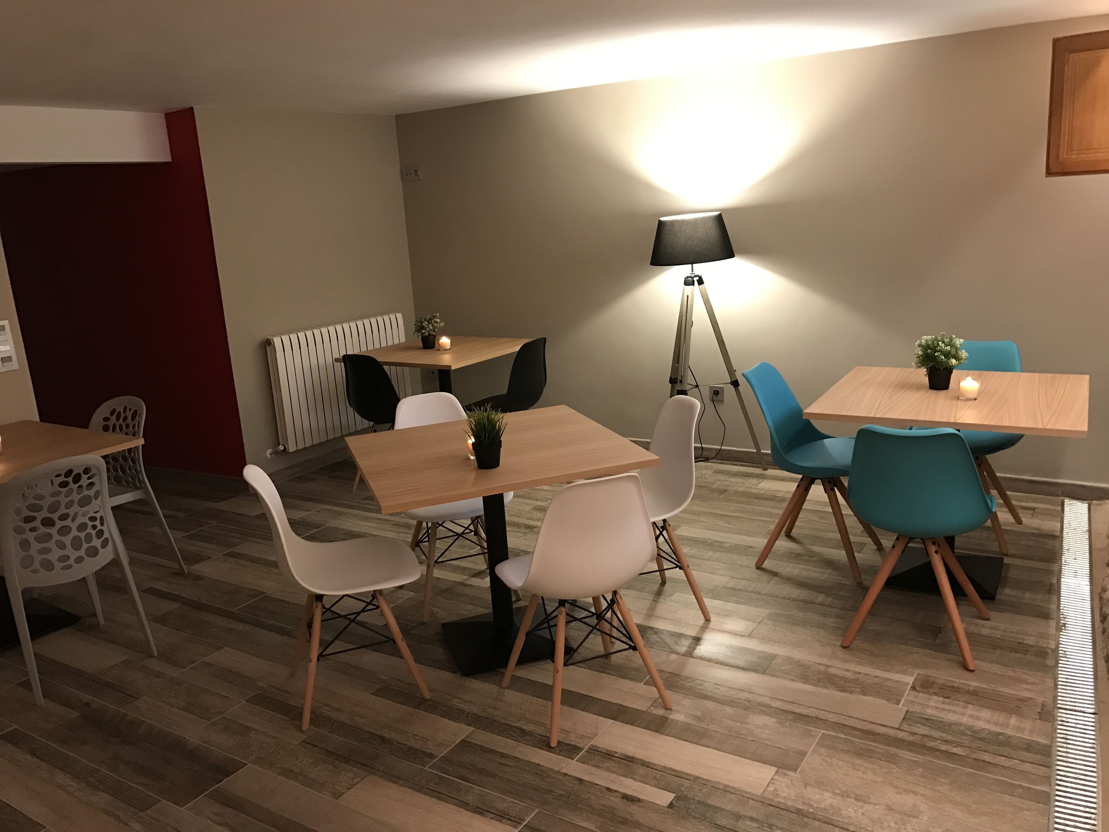 A modern dining area with wooden tables and chairs, a floor lamp, and a potted plant.
