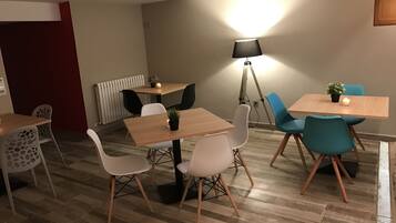 A modern dining area with wooden tables and chairs, a floor lamp, and a potted plant.