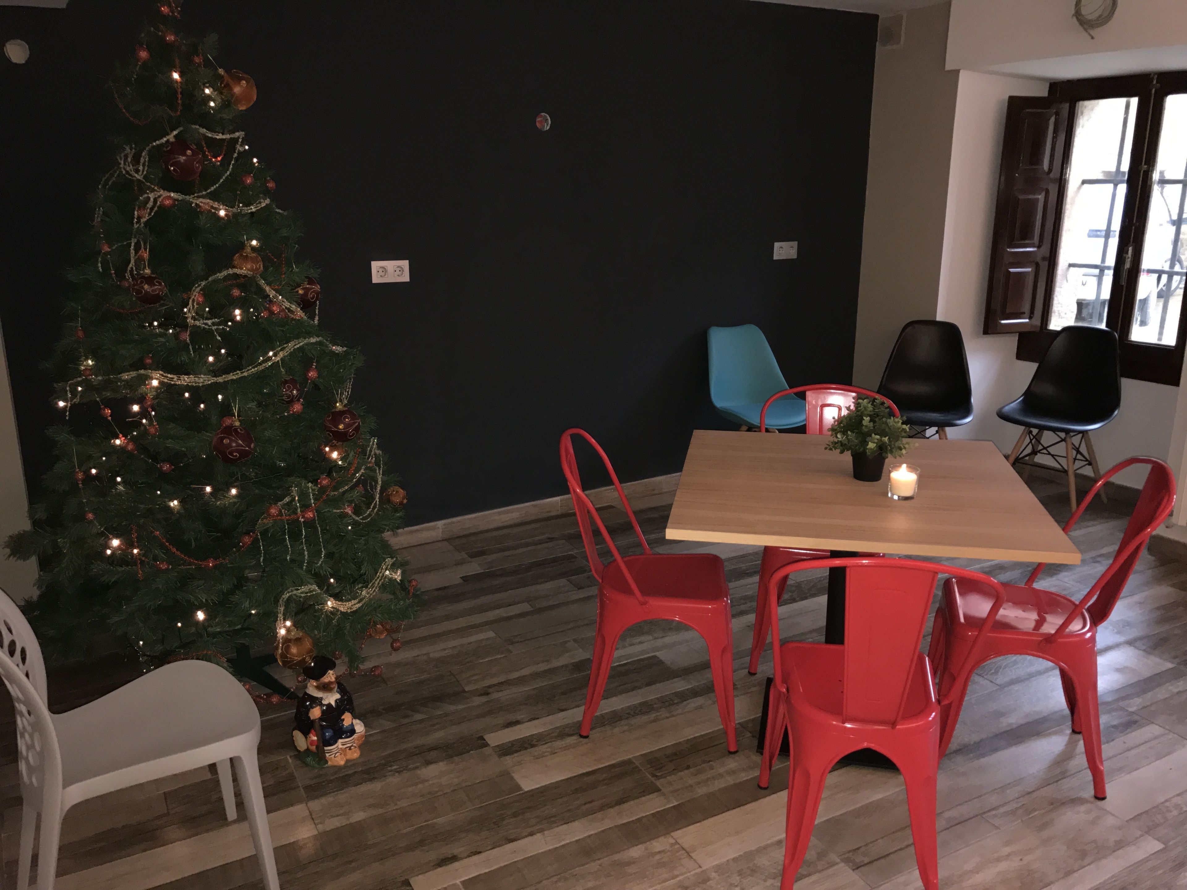 Un área de comedor con una mesa de madera y sillas rojas, un árbol de Navidad con luces y adornos, y una ventana con vistas.