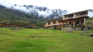A two-story building with a balcony, surrounded by a grassy area and mountains in the background. - Gocta Andes Lodge (Cocachimba)