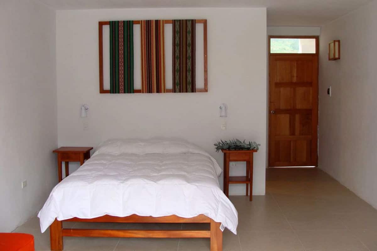 A bedroom with a wooden bed, a small bedside table, a wall-mounted artwork, and a door leading to another room.